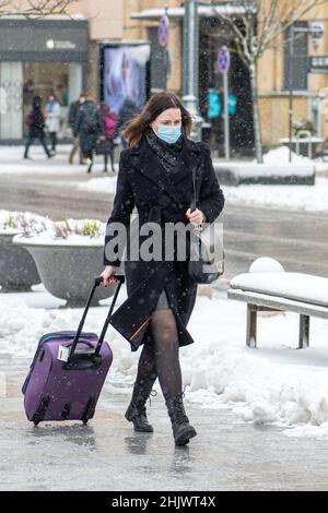 Elegante bella ragazza business indossare giacca nera con maschera medica protettiva e bagagli a piedi per strada durante Covid o Coronavirus Foto Stock