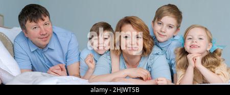 Felice famiglia caucasica si trovano in camera da letto e sorridere. Vestiti di blu stanno divertendosi insieme. Genitori e figli due figli e una figlia carina Foto Stock