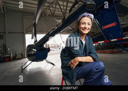 Bella bruna sorridente ingegnere airframe seduto nel garage dell'aviazione Foto Stock