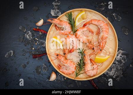 gamberetti freschi su ghiaccio con erbe e spezie limone peperoncino rosmarino aglio su piatto di legno, gamberi bolliti gamberi cotti nel ristorante di pesce Foto Stock