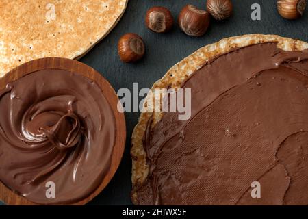 Vista dall'alto del cioccolato alle nocciole, frittelle francesi o crepes e nocciole su sfondo di pietra nera Foto Stock