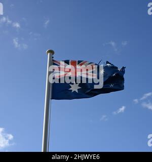 Bandiera australiana appesa a un palo di bandiera metallica, con cielo blu brillante e nuvole di bianco chiaro sullo sfondo Foto Stock