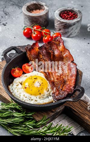 Colazione inglese con uova fritte e pancetta in padella di ghisa. Sfondo grigio. Vista dall'alto Foto Stock