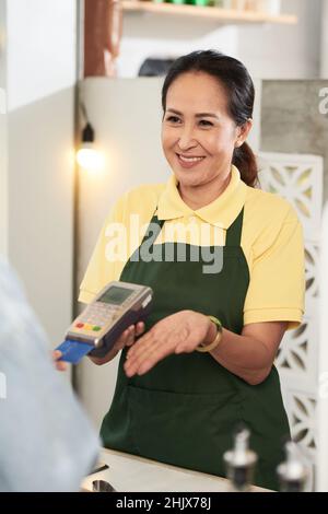 Allegro barista di mezza età che accetta il pagamento per caffè e cibo Foto Stock