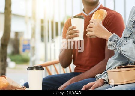 La giovane coppia si diverte a gustare caffè e sandwich quando si siede all'aperto Foto Stock