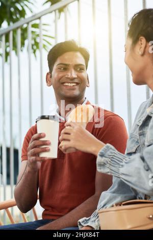 Buon giovane uomo che gode di una data romantica con la ragazza, stanno mangiando cibo di strada e parlando Foto Stock