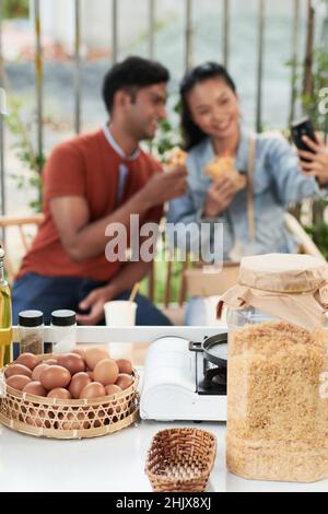 Grande vasetto di formaggio grattugiato e uova di pollo fresche sul banco del caffè, giovane coppia che mangia al tavolo in background Foto Stock