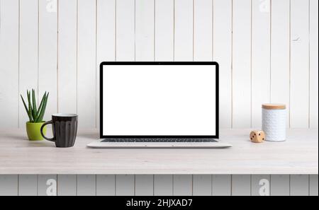 Lapop sulla scrivania con schermo bianco isolato per la promozione di mockup, app o pagine Web. Parete bianca in legno sullo sfondo Foto Stock