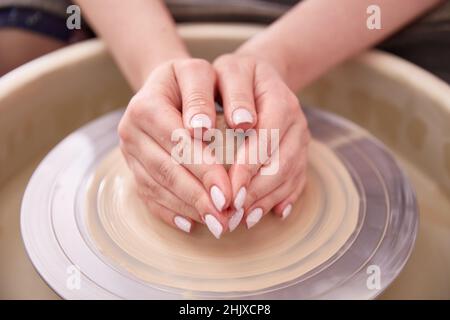 Le mani femminili ben curate scolpiscono una tazza di argilla dietro la ruota di un vasaio Foto Stock