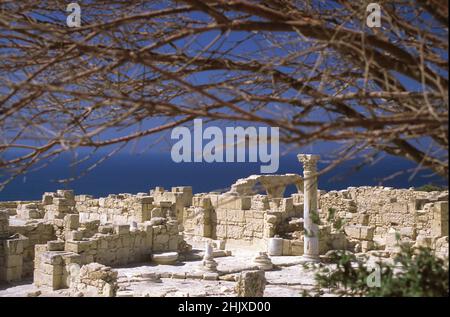 Resti del palazzo vescovile, antica Kourion, Episkopi, distretto di Limassol, Cipro: Mura tumbled, Archi e una colonna dorica contro il blu del Mediterraneo Foto Stock