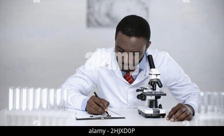 lo scienziato afro-americano scrive su appunti vicino al microscopio Foto Stock