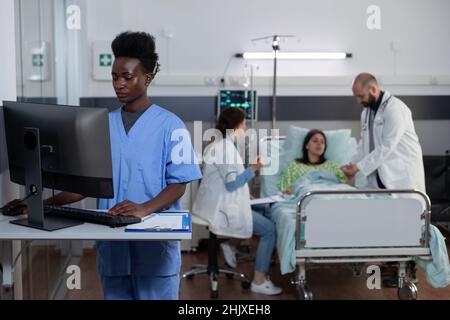 Infermiera con personal computer per completare la cartella di ammissione del paziente e leggere l'anamnesi medica nel reparto ospedaliero. Medico che mette il pulsossimetro sul dito del paziente mentre il medico scrive sulla clipboard. Foto Stock