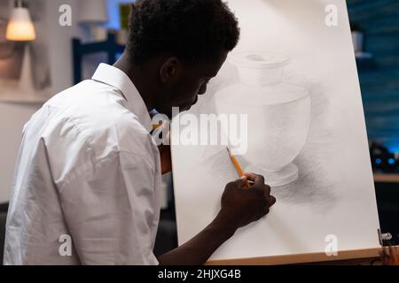 Giovane artista che disegna vasi facendo ombre usando matita grafica professionale che lavora a ilustration creativo per lezione d'arte. Concentrato di pittura uomo studente su tela disegno di schizzo Foto Stock