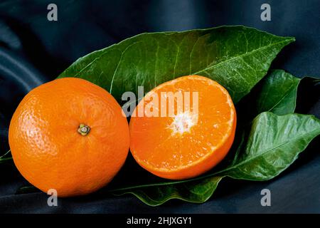 Primo piano di clementina o mandarino fresco e tagliato a metà con foglia verde su sfondo scuro Foto Stock