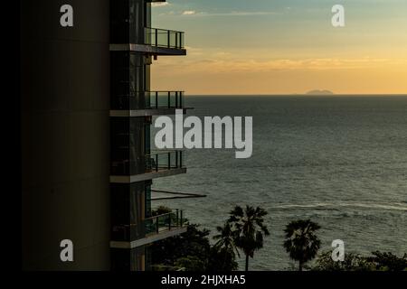 Un edificio alto e moderno con balconi che si affacciano sul cielo del tramonto e sul mare con la luce arancione del tramonto, spazio per la copia e il design, paesaggio ima Foto Stock