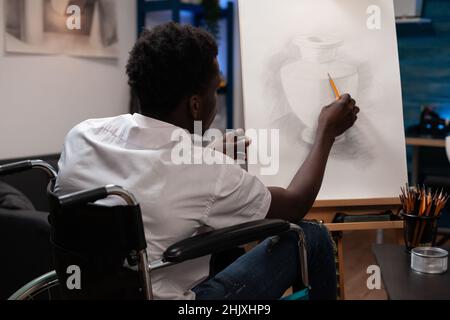 Studente d'arte con disabilità che disegna l'ilustrazione dei vasi lavorando all'ombra utilizzando strumenti grafici professionali durante la classe creativa. Il giovane illustratore che si ispira a tela in studio Foto Stock