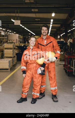 Ritratto di colleghi sorridenti di sesso maschile e femminile in uniforme in piedi presso il magazzino di fabbrica Foto Stock