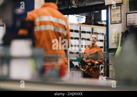 Lavoratore femminile in uniforme discutere con collega maschio in fabbrica Foto Stock