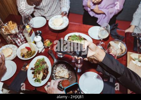 Immagine ritagliata di una donna che fotografa su smartphone mentre cena con gli amici al bar Foto Stock