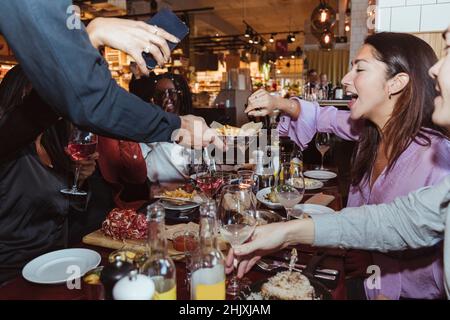 Immagine ritagliata del cameriere che serve cibo e bevande ai clienti al tavolo Foto Stock