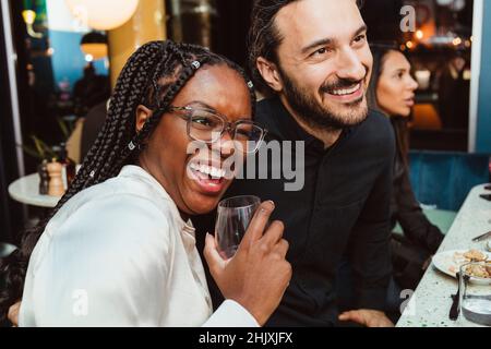 Giovane donna che ride mentre si siede da un amico maschio in bar post-lavoro Foto Stock