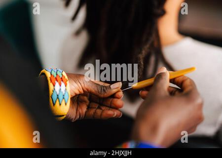 Immagine ritagliata del barbiere femminile che fa i locs con il gancio del crochet nel salone Foto Stock