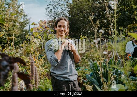 Ritratto di socio agricolo maschile sorridente con pianta in giardino urbano Foto Stock