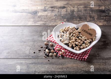Legumi assortiti non cotti in piastra a forma di cuore su tavola rustica in legno Foto Stock