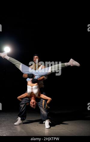 ballerini europei hip-hop donna e uomo che mostrano diversi trucchi e movimenti mentre ballano in studio su sfondo nero, sul palco, flessibile e spor Foto Stock