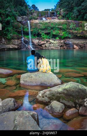 giovane coppia isolata seduta su roccia con sfondo incontaminato cascata al mattino in immagini foreste è preso a lyngksiar cascate cherrapunjee meghalay Foto Stock