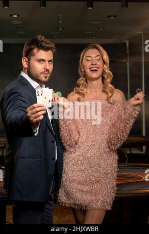 Donna felice e uomo fiducioso vincere poker in piedi vicino al tavolo da gioco Foto Stock