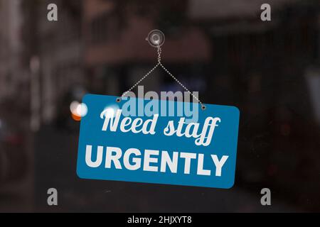 Primo piano su un segno rosso e bianco in una finestra con scritto il messaggio - bisogno di personale urgente -. Foto Stock
