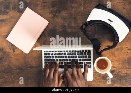 Scrivania uomo in legno scuro scrivente su computer portatile con visore VR per notebook e coffe Cup - scatto dall'alto. Foto di alta qualità Foto Stock