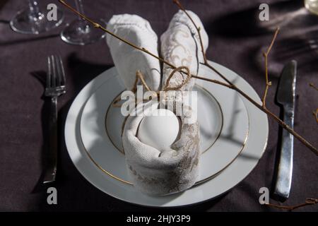 Idea della cartella del tovagliolo. Tavolo di Pasqua. Pasqua tavolo impostazione con uovo in tovagliolo grigio coniglio di Pasqua su uno sfondo di lino marrone. Spazio di copia, vista dall'alto, Foto Stock