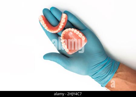 La mano del medico in un guanto blu tiene una dentiera. Protesi dentaria nelle mani del medico primo piano. Dentista che tiene ponte dentistico in ceramica. Denti Foto Stock