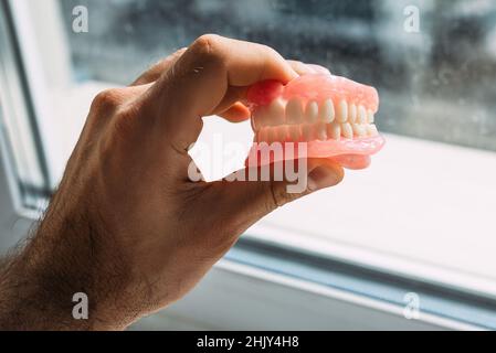 Un uomo anziano tiene una dentaria. Un uomo tiene le dentiere nelle sue mani. Dentiera rimovibile flessibile. Falsi denti. Impianto. Ortodonzia. Vecchiaia. Teet Foto Stock