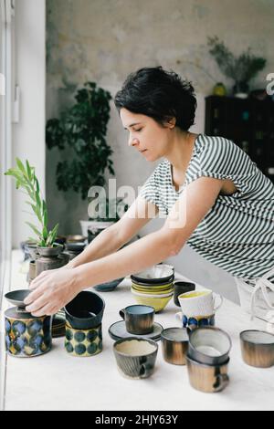 Craftswoman arrangiare su tavola in ceramica negozio Foto Stock