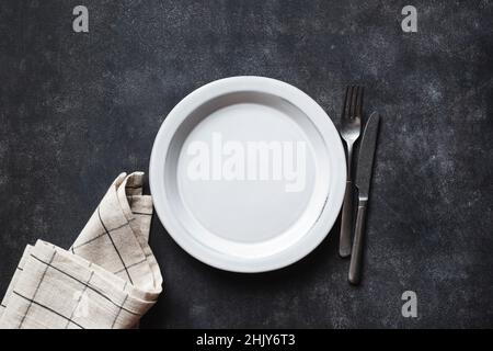 Piatto vuoto, posate e biancheria da tavola su fondo piano in cemento nero. Vista dall'alto dello spazio di copia. Tavolo da cucina Foto Stock