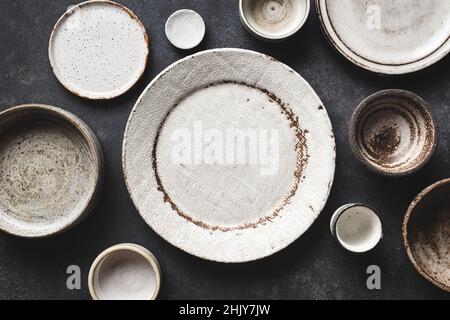 Piatti e ciotole in ceramica artigianali moderni e alla moda su sfondo tavola in cemento. Vista dall'alto spazio di copia. Utensili da cucina Foto Stock