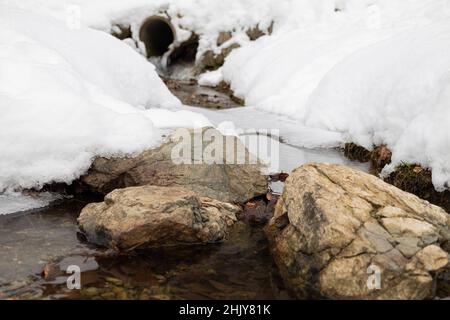 Germania, Foresta Nera - Nonnenmattweiher, pietre in ruscello ghiacciato con sfondo nevoso Foto Stock