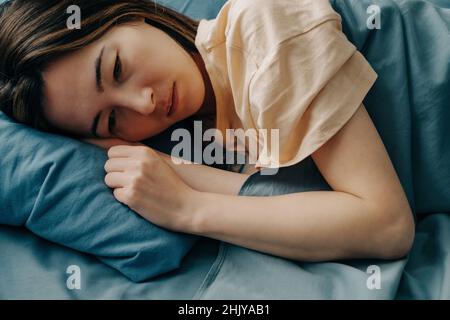 Una giovane donna triste si trova a letto e non può dormire. Foto Stock