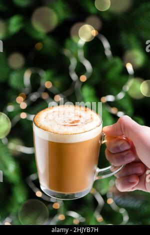 Tazza di caffè caldo Cappuccino con sciroppo di pan di zenzero in mano maschile davanti all'albero di Natale. Drink di vacanza Foto Stock