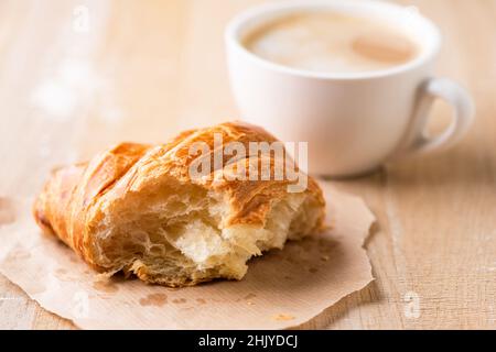 Metà mangiato croissant francese fresco e una tazza di caffè su sfondo, tavolo di legno sfondo. Pausa caffè nella caffetteria Foto Stock