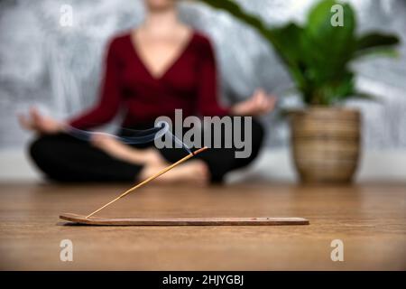 Donna membful meditating a casa con i bastoni di incenso brucianti, sedersi nella posa del loto. Tenere le mani in grembo con i palmi rivolti verso l'alto. Foto Stock