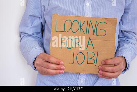 Un uomo disoccupato che tiene un cartello con iscrizione ALLA RICERCA DI UN LAVORO. Concetto di perdere lavoro e di cercare un nuovo. Ha problemi finanziari. Foto Stock