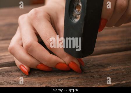 Una donna con un manicure rosso martella un chiodo. Foto Stock
