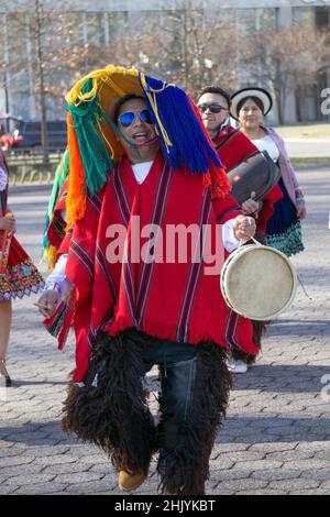 Un ecuadoriano New Yorker suona la batteria e danze indossando un cappello colorato con lunghe corde. In un parco a Queens, New York City. Foto Stock