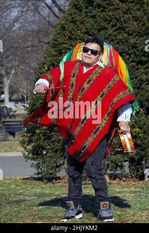 Un ecuadoriano New Yorker suona la batteria e danze indossando un cappello colorato con lunghe corde. In un parco a Queens, New York City. Foto Stock