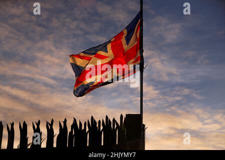 Il sole sorge sopra Belfast orientale mentre la bandiera dell'Unione soffia nel vento. Foto Stock