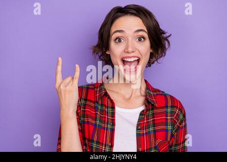 Foto di divertente giovane bob hairdo lady yell mostra rock segno indossare camicia rossa isolato su sfondo di colore viola Foto Stock